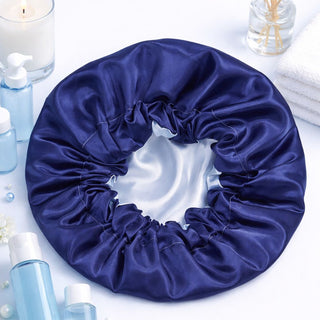 Navy blue satin hair bonnet on a white surface with skincare products and a candle.