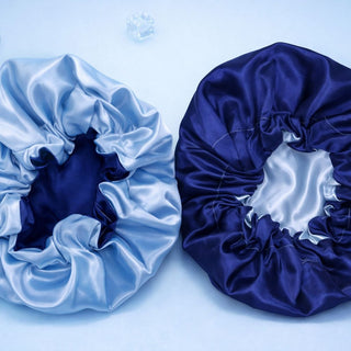 Two satin hair bonnets, one white and one blue, on a light blue background with decorative elements.